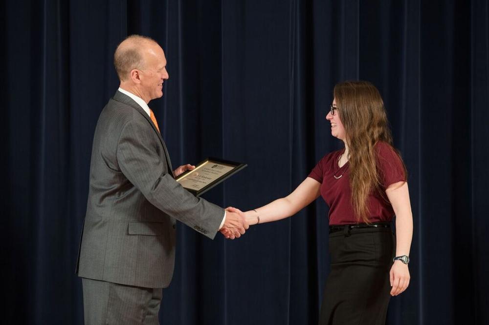 Doctor Potteiger shaking hands with an award recipient in a maroon shirt